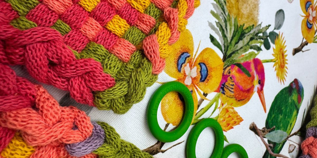 Close-up of coral, pink and green woven loops for homemade pot holders beside a tote printed with birds and flowers